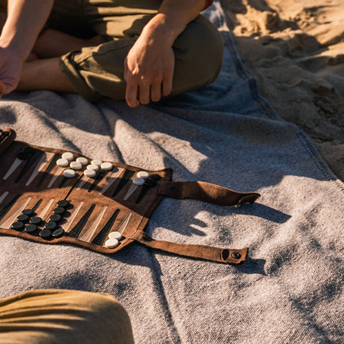 Zwei Personen im Sand auf einer decke spielen das backgammon deluxe Reisespiel